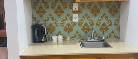 A small kitchen with wooden cabinets, a countertop, a sink, and a kettle.