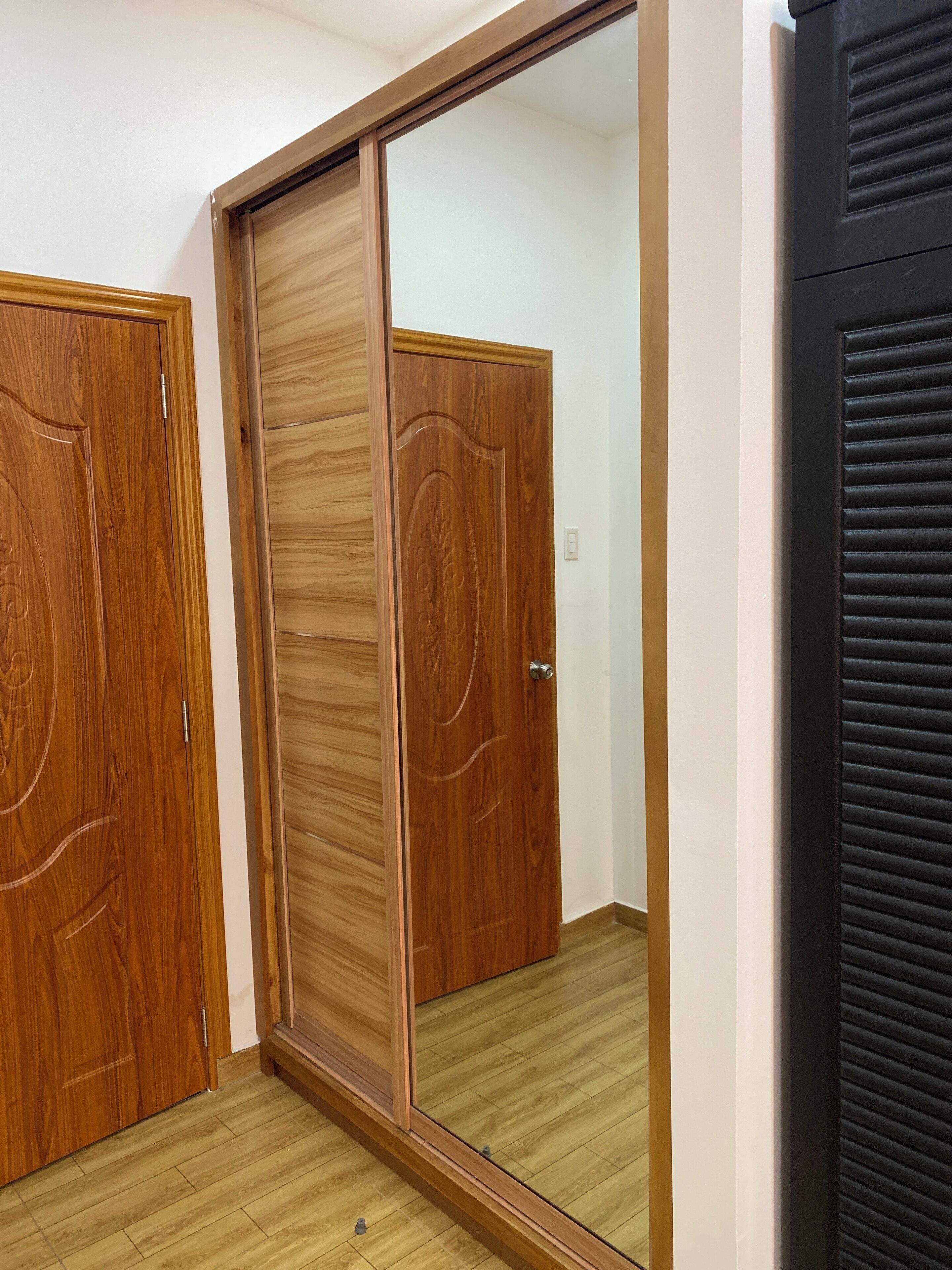 A room with a wooden wardrobe, a mirrored closet door, and a black door with a vent.