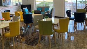A modern dining area with a mix of yellow and green chairs, a central table, and a ceiling with wooden panels and hanging lights. - July Apartments (Philipsburg)