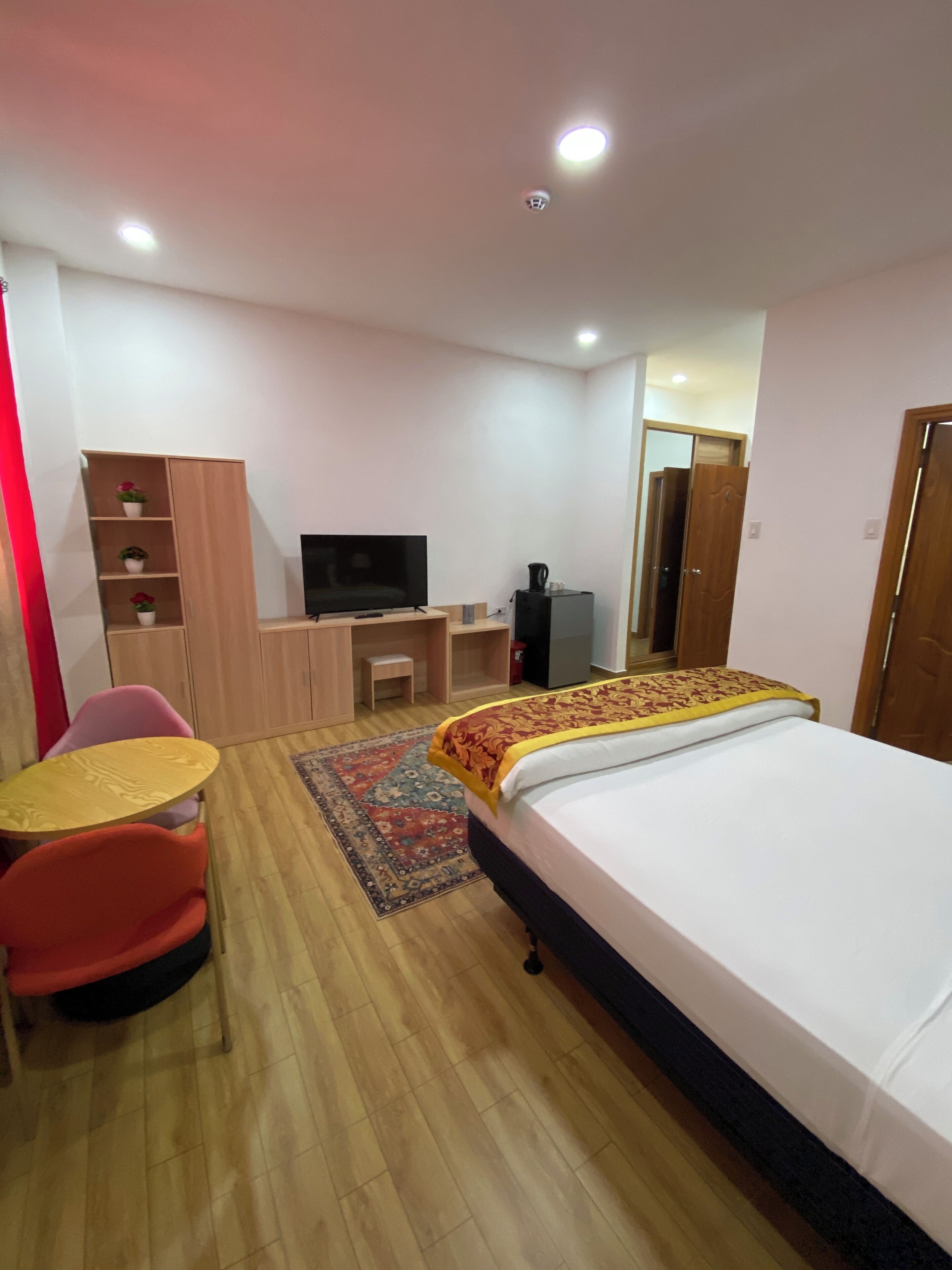 A hotel room with a bed, a desk, a television, a wardrobe, and a small table with chairs.
