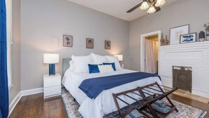 A bedroom with a bed, bedside tables, a ceiling fan, a fireplace, and framed pictures on the wall. - Location, Location, Location (Lexington)