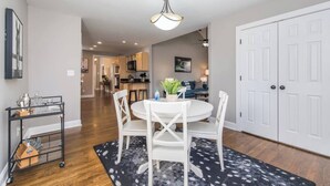 A dining area with a round table, white chairs, a chandelier, and a kitchen in the background. - Location, Location, Location (Lexington)