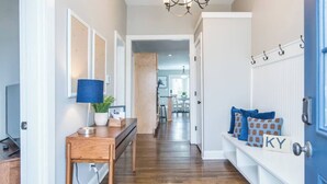 A hallway with wooden flooring, a chandelier, a bench with cushions, and a wall-mounted coat rack. - Location, Location, Location (Lexington)