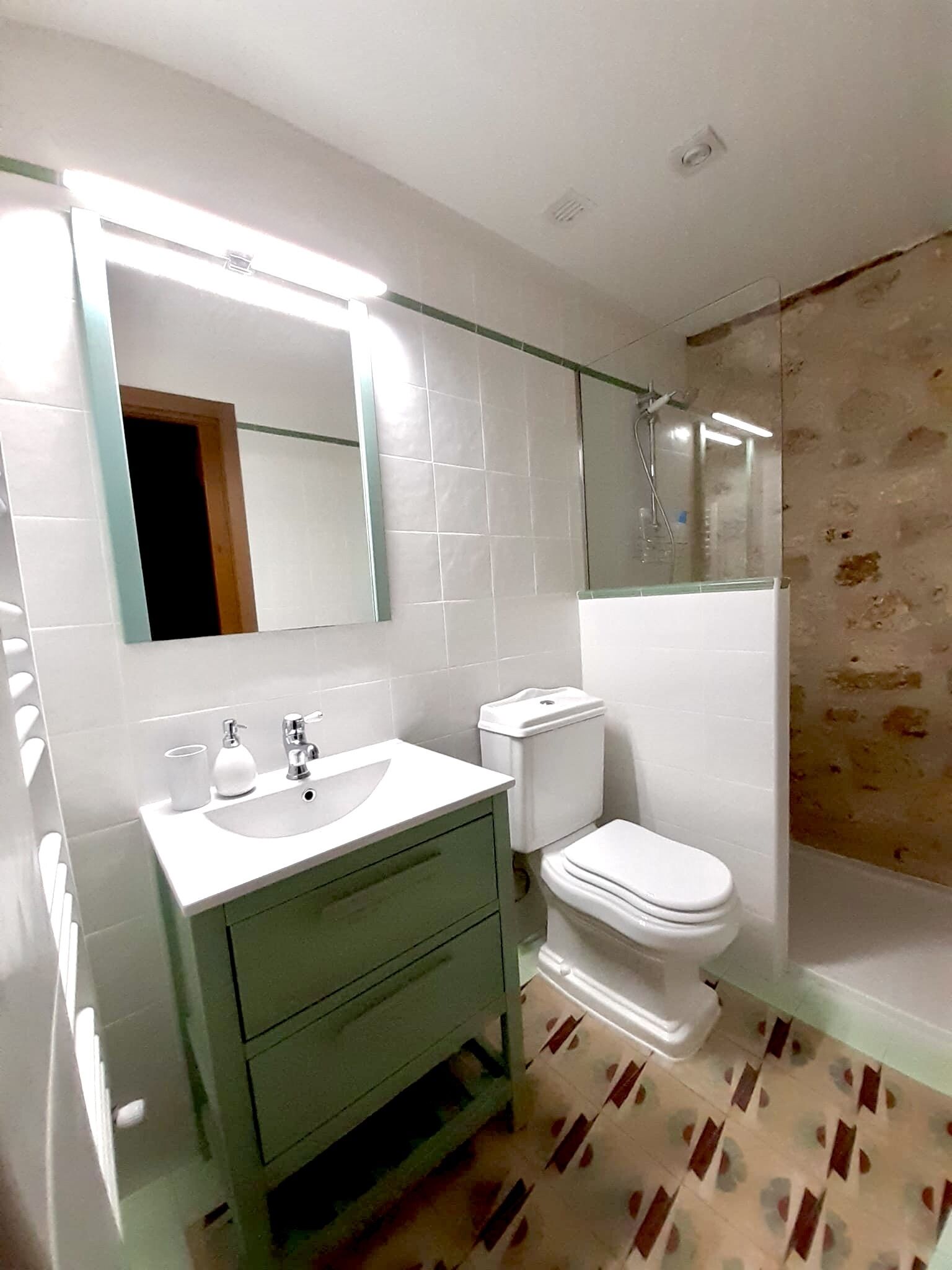 A modern bathroom with a white sink, green vanity, a toilet, and a glass shower enclosure.