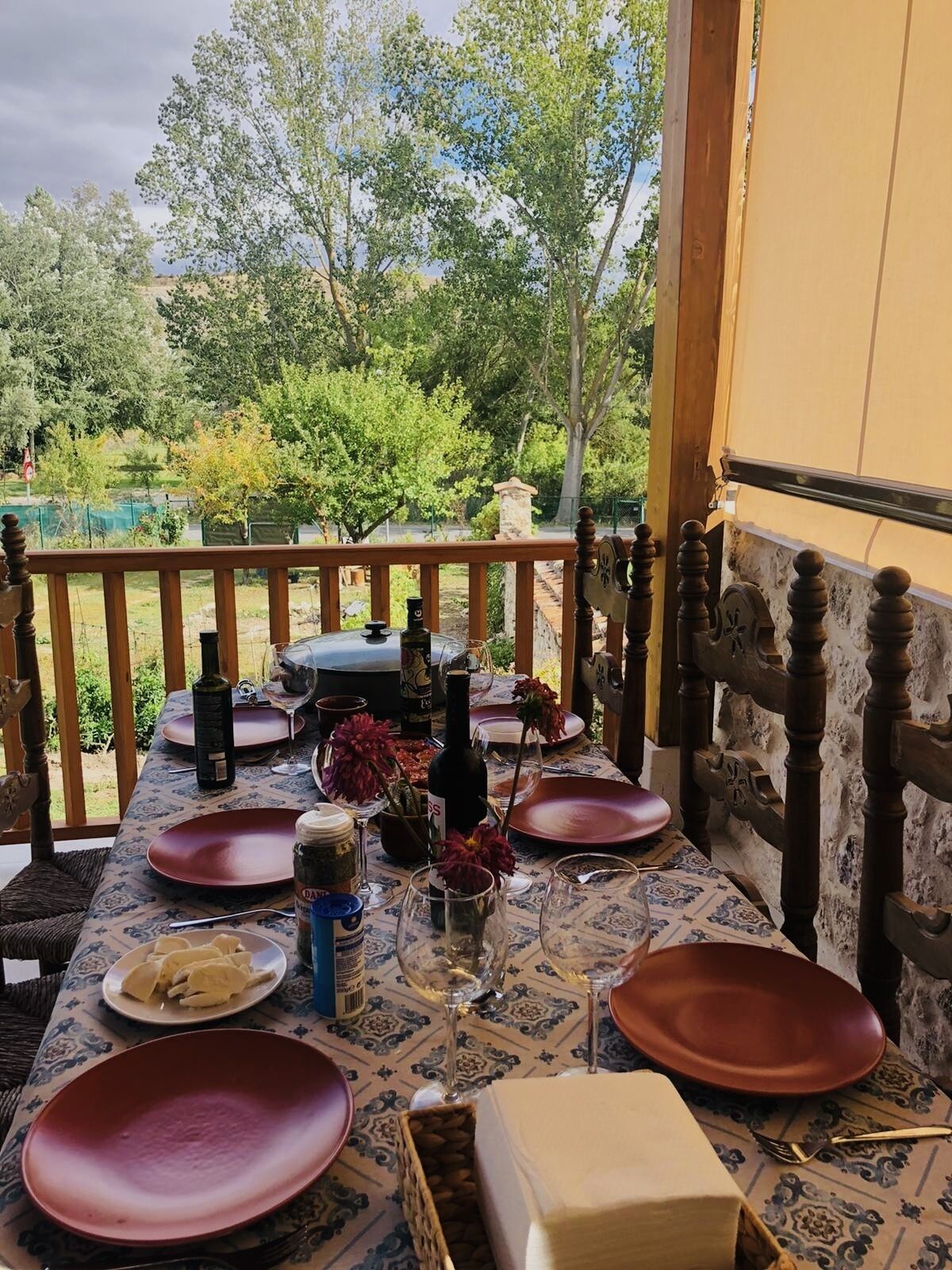 Een eettafel buiten gedekt, met rode borden, wijnglazen en flessen.