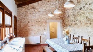 A rustic room with a stone wall, wooden beams, a dining table with chairs, a bench, and a window with wooden shutters. - Charming accommodation, next to Ribera del Duero and Hoces del Duratón (aldeasoña)
