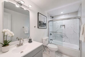 Un baño moderno con un espejo grande, un lavabo, un inodoro y una ducha con mampara de vidrio.
