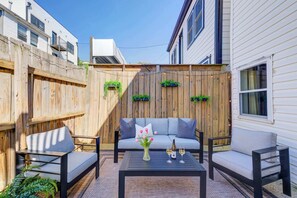 Une terrasse avec un canapé, deux fauteuils, une table basse et un petit espace jardin agrémenté de plantes.