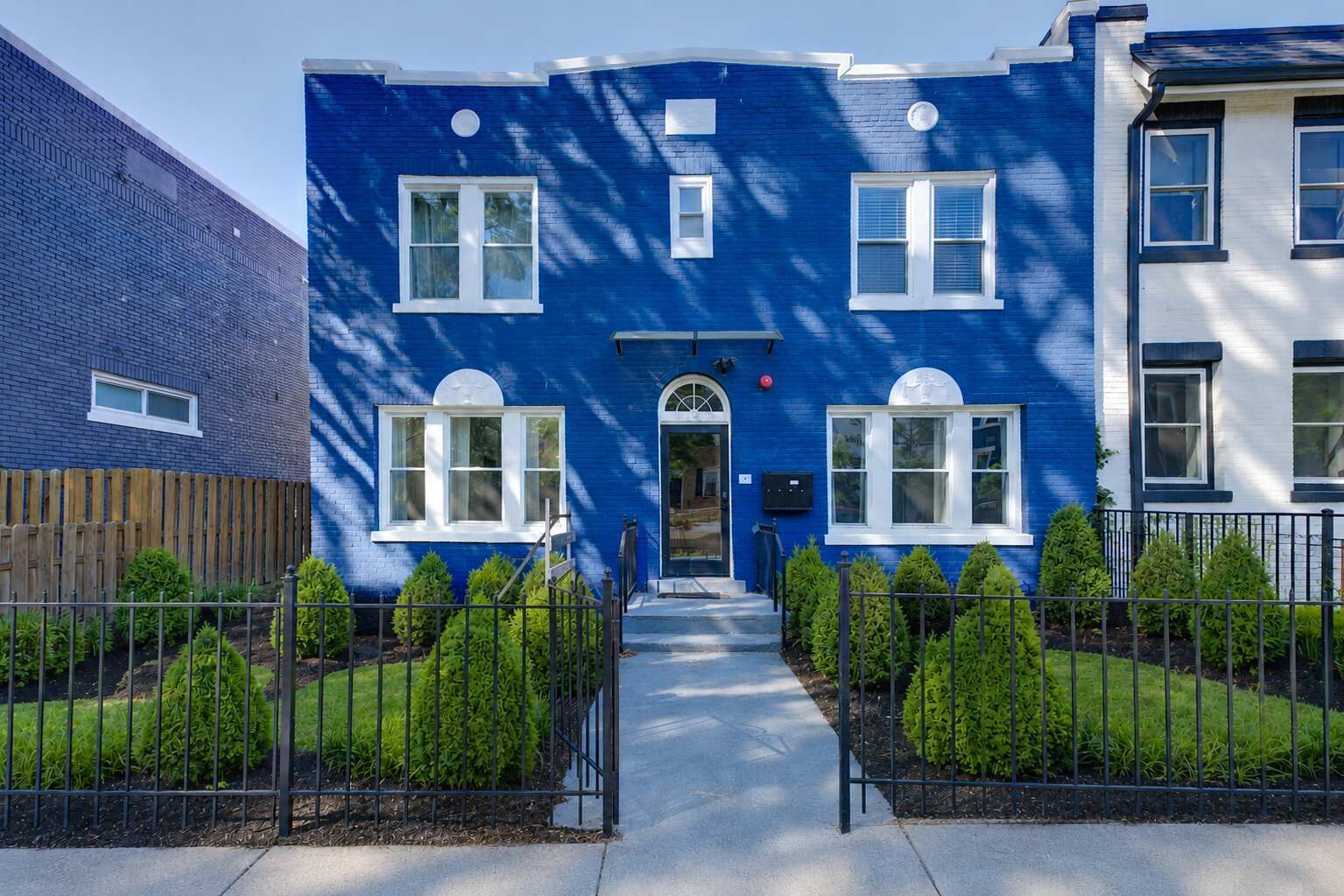 A two-story building with a blue exterior, a wooden fence, and a well-maintained garden with hedges.