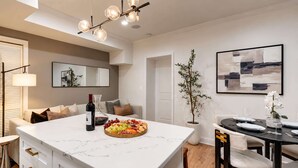 Eine moderne Küche mit einer Marmorinsel, einem Essbereich mit schwarzem Tisch und Stühlen sowie einem Wohnbereich mit Sofa und Pflanze.