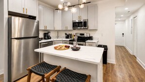Una cocina moderna con electrodomésticos de acero inoxidable, una isla de mármol y una silla tejida negra.