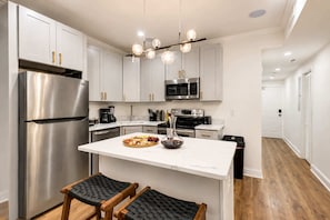 Una cocina moderna con electrodomésticos de acero inoxidable, una isla de mármol y una silla tejida negra.