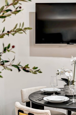 Une table à manger est dressée avec des assiettes, des couverts et des verres à vin, et un téléviseur est fixé au mur au-dessus.
