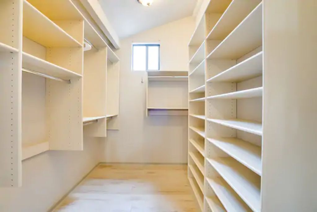 A narrow walk-through closet with multiple shelves and a small window at the end.
