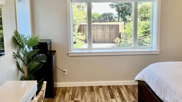 A bedroom with a large window, wooden flooring, a bed, a desk, and a ceiling fan. - Kate Sessions Park Large Private Entry Room (San Diego)