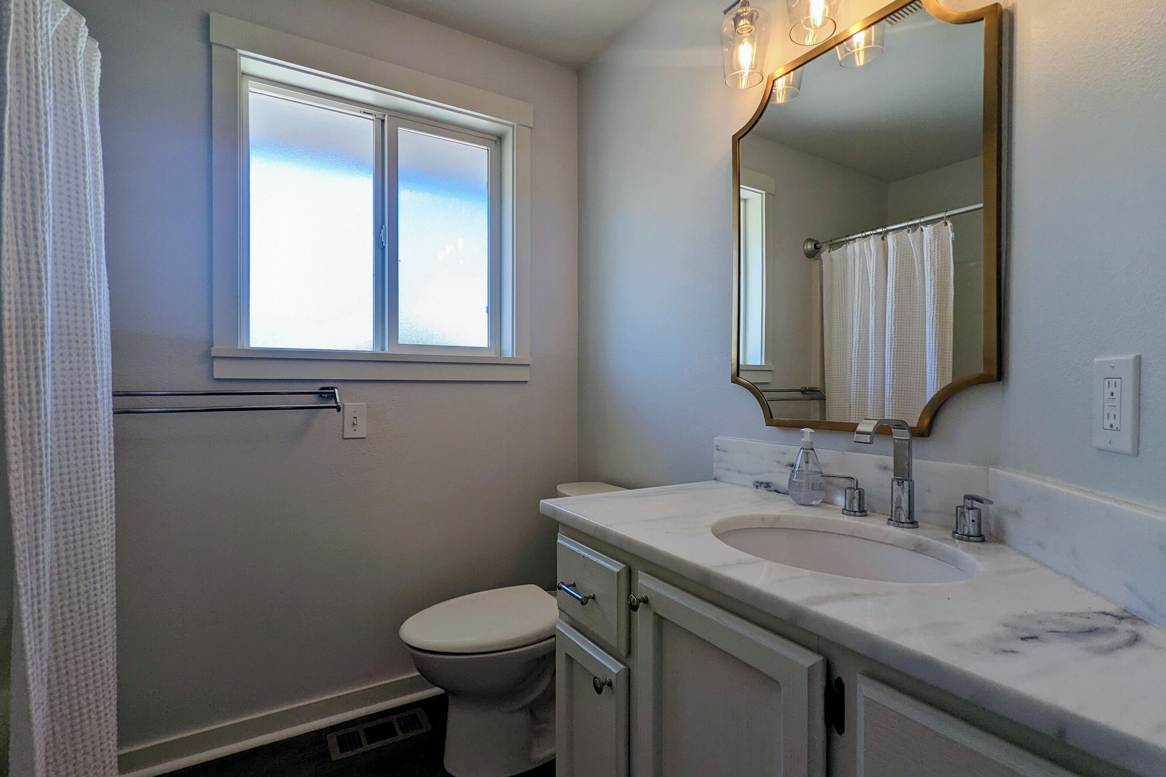 A bathroom with a toilet, a sink, a mirror, and a window.