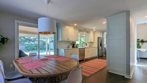 A modern kitchen with white cabinets, a dining area with a round table and chairs, and a view of the outdoors. - Arioso House - Style Inspired by Classical Music! (Newberg)