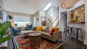A living room with a sofa, chairs, a coffee table, a patterned rug, and a staircase leading to a kitchen. - Arioso House - Style Inspired by Classical Music! (Newberg)