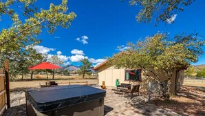 A patio area with a hot tub, outdoor furniture, and a small building with a window.