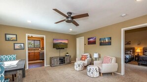 A spacious living area with a ceiling fan, a dining table, and a kitchen in the background.