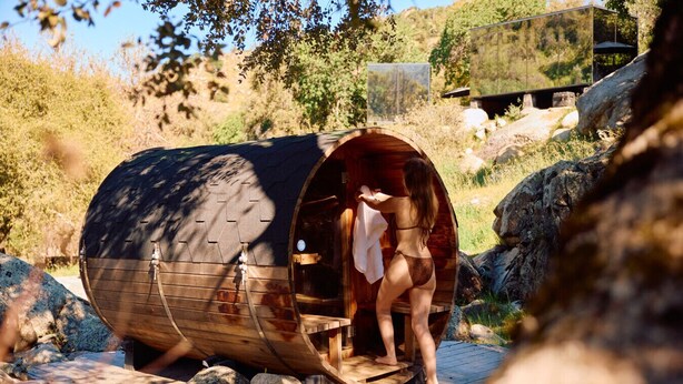 A wooden sauna with a curved roof, a wooden bench, and a person stepping out. - Paradise Ranch Inn - Mindful Tent (Three Rivers)