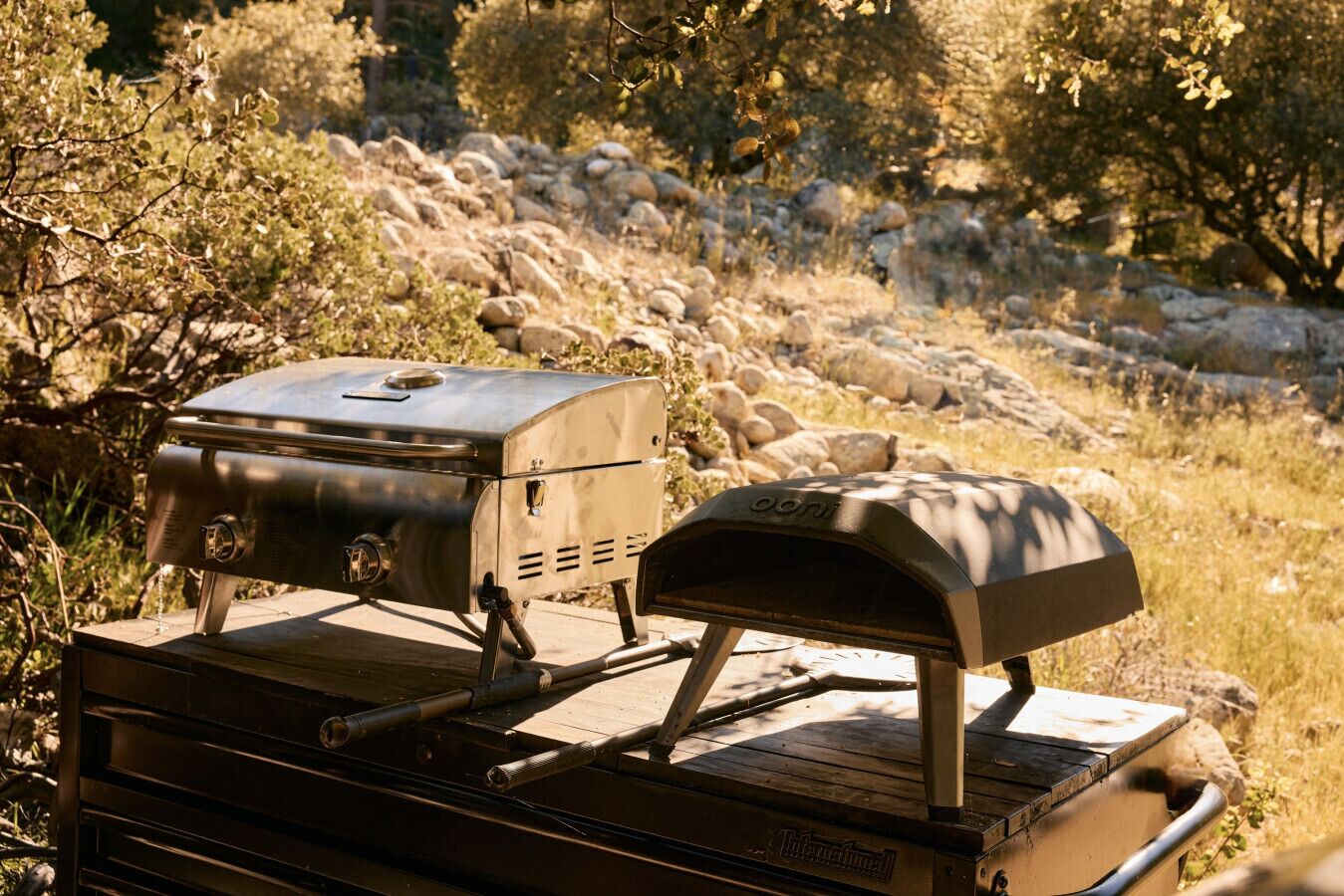 A portable grill with a built-in cooler and a chimney, placed on a wooden surface outdoors.