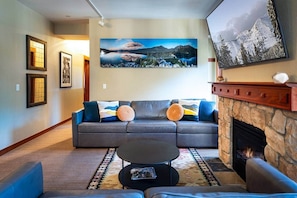 Un salon avec un canapé, une table basse, une cheminée et des tableaux encadrés accrochés au mur.