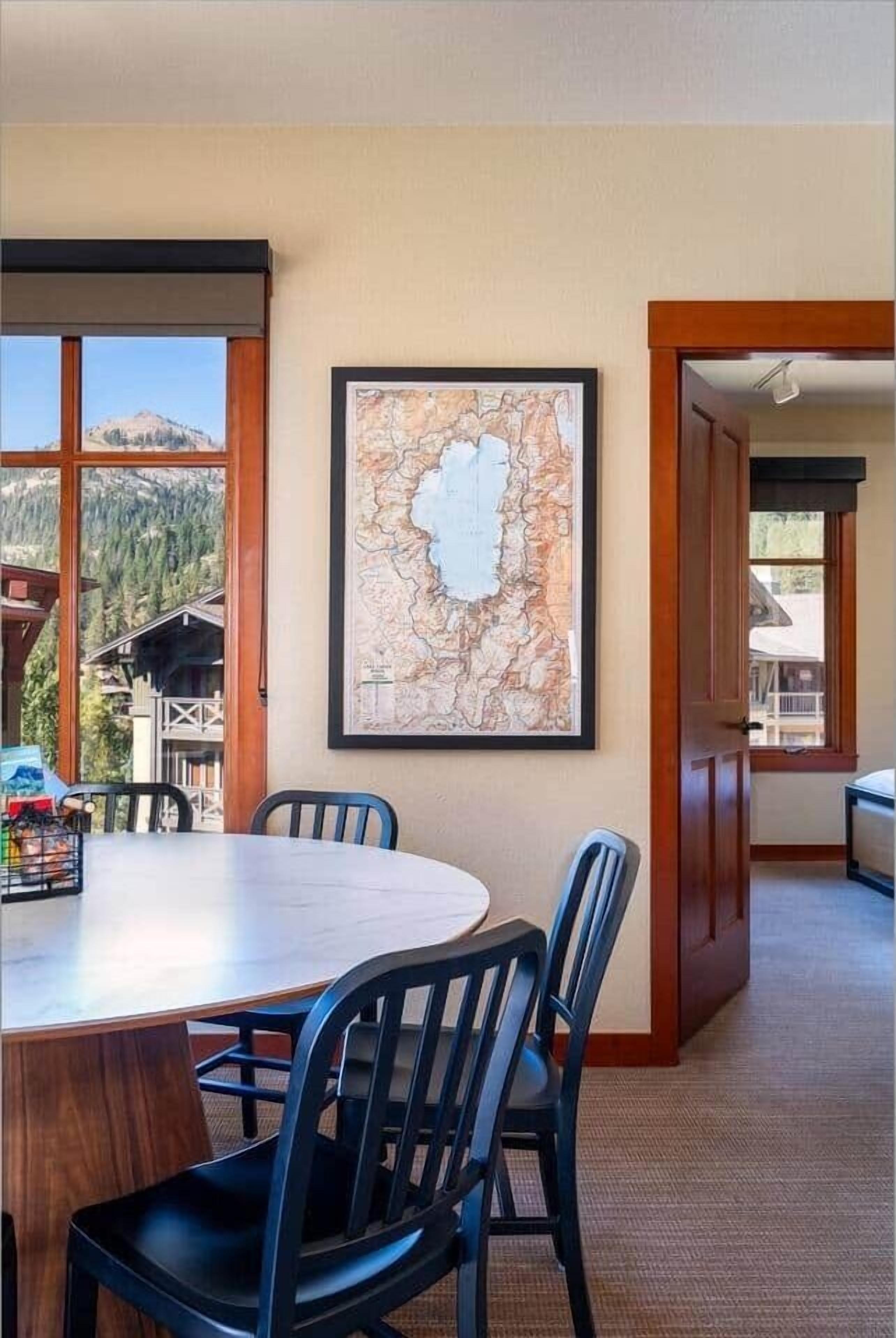 Un espace repas avec une grande table et des chaises, une carte encadrée accrochée au mur et une vue sur les montagnes par de grandes fenêtres.