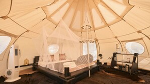 Een tent met een bed, een ventilator en een tafel met spullen.