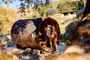 A wooden sauna with a curved roof, a wooden bench, and a person stepping out. - Paradise Ranch Inn - Liberated Tent (Three Rivers)