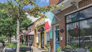 Una calle con mesas al aire libre, un edificio con el rótulo 'HOT HEADS' y un rótulo que dice 'Barefoot Studio'.
