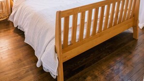 Un dormitorio con cama de madera, ventilador de techo, ventana con vistas y un espejo decorativo en la pared.