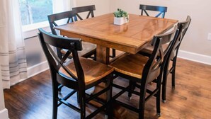 Un comedor con una mesa de madera y cuatro sillas, un reloj de pared y una ventana con cortinas.
