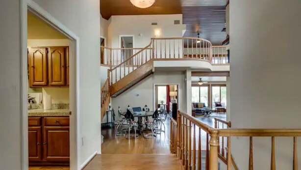Un interior espacioso con una escalera de madera que conduce a un segundo piso, un comedor con mesa y sillas, y armarios de madera en la cocina.