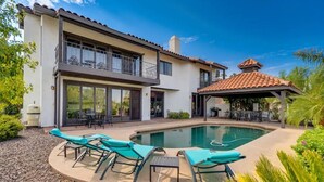 Una casa de dos pisos con piscina, mobiliario exterior y un patio cubierto.
