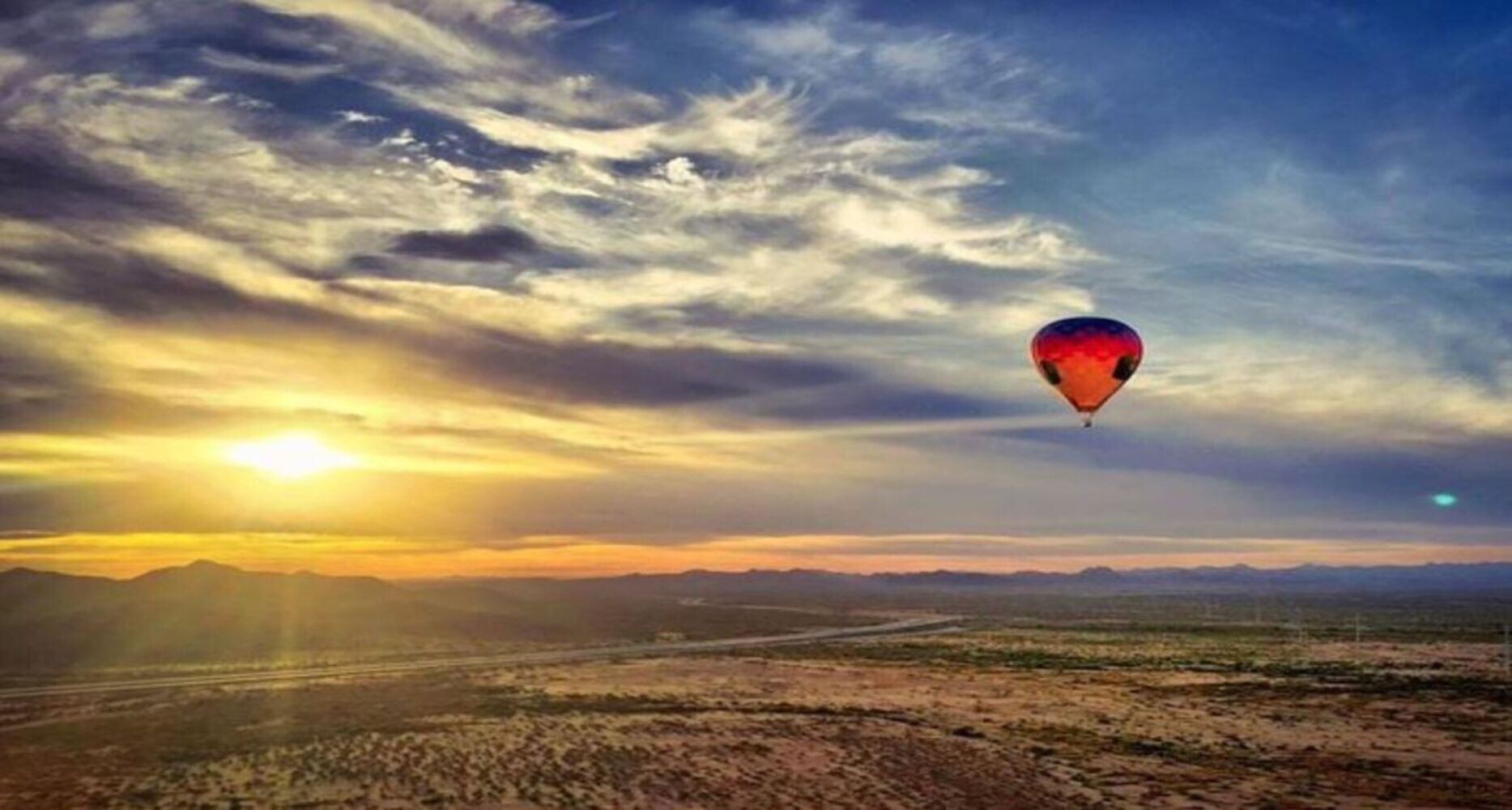 Een luchtballon boven een landschap met bergen en een zonsondergang.