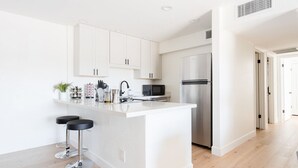 Una cucina moderna con mobili bianchi, un frigorifero in acciaio inossidabile, un forno a microonde e due sgabelli da bar.