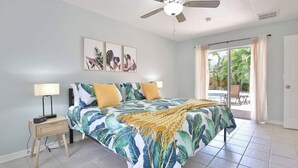 A bedroom with a bed, a nightstand, a ceiling fan, and a view of the outdoors.