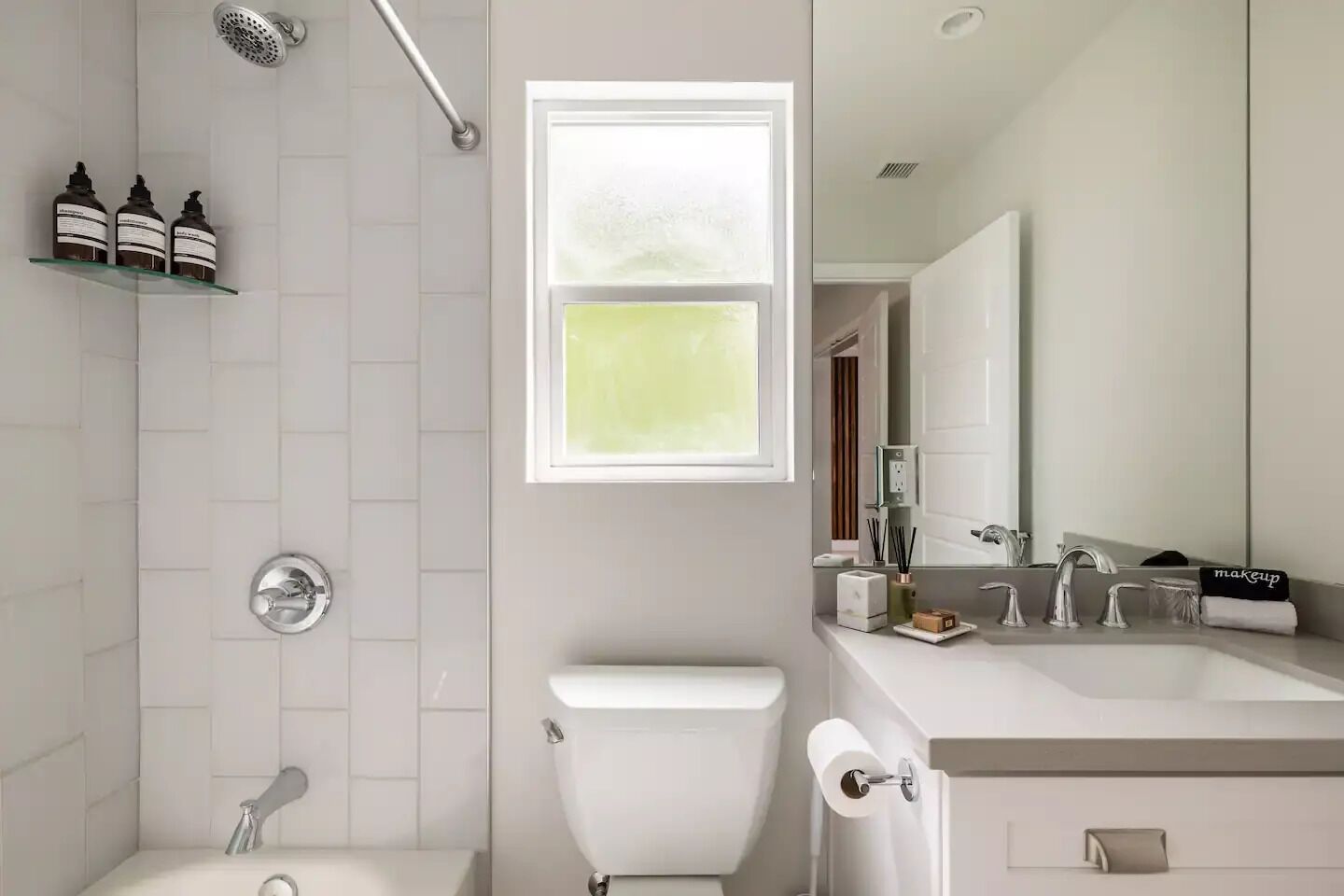 Un bany modern amb dutxa, vàter i rentapel. Hi ha una finestra que deixa entrar llum natural i un mirall sobre el rentapel.