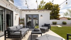 Une terrasse extérieure avec un canapé gris, deux fauteuils, une petite table et des guirlandes lumineuses.