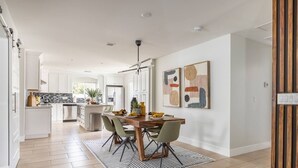 Une cuisine moderne avec des meubles blancs, un îlot central et un coin repas comprenant une table et des chaises en bois.