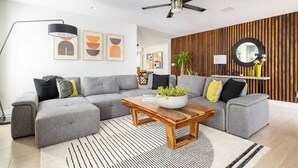 Un salon moderne avec un canapé d’angle gris, une table basse en bois et un tapis rayé noir et blanc.