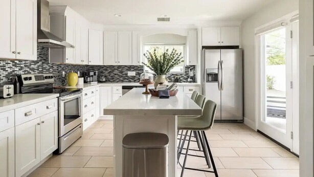 Une cuisine moderne avec des meubles blancs, un îlot central et un réfrigérateur en acier inoxydable.