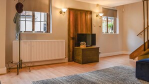 Une pièce avec un radiateur, une porte en bois, un téléviseur posé sur un meuble et un escalier.