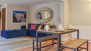 Un salon moderne avec un canapé bleu, des coussins colorés, une table basse en bois et un miroir doté d’un cadre original.