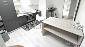 Una cocina moderna con horno integrado, un lavamanos y un lavavajillas. Hay una mesa de comedor con un banco, una silla blanca y una lámpara colgante.
