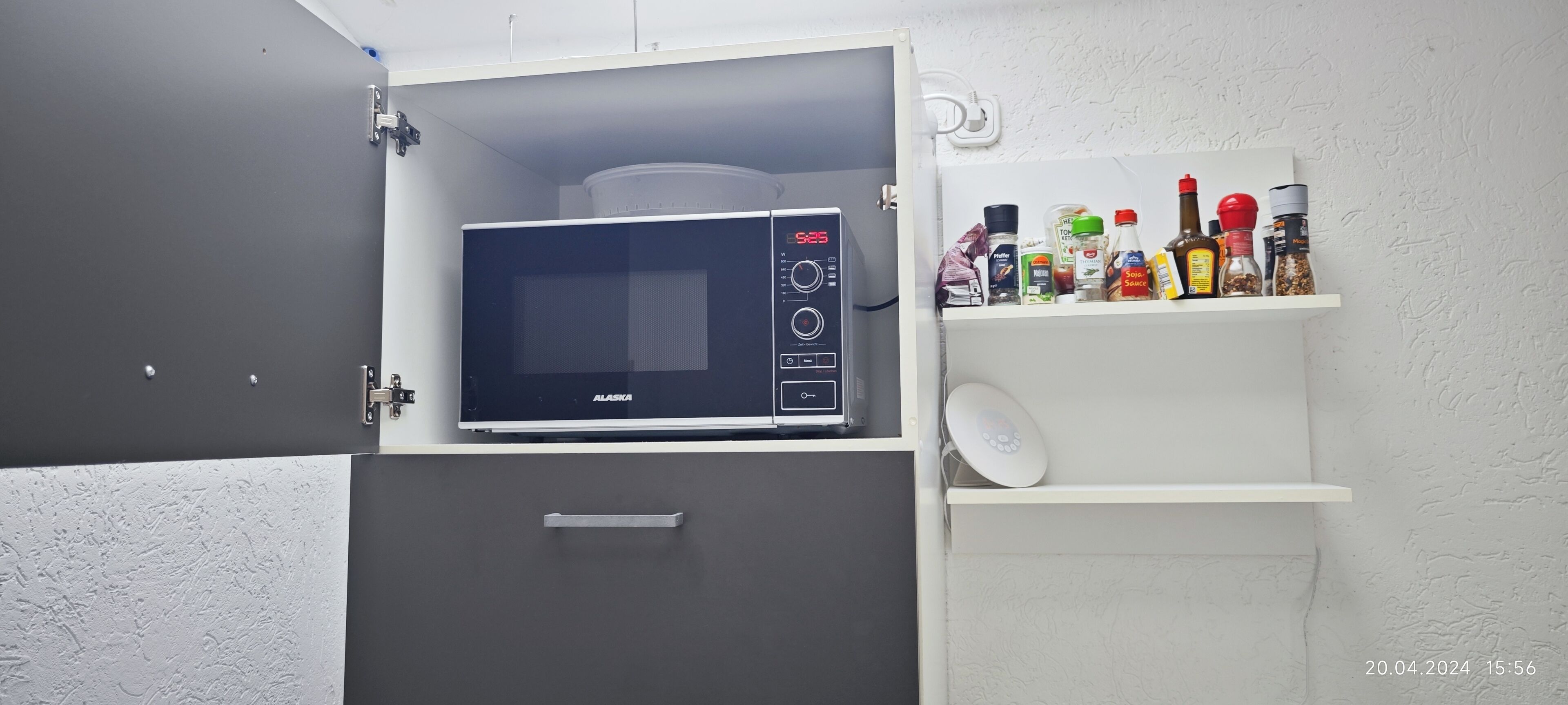 A kitchen with a microwave, a shelf with condiments, and a white cabinet.