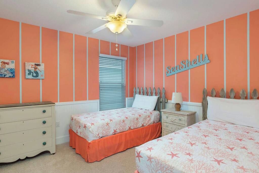 A bedroom with two beds, a dresser, a ceiling fan, and a window with blinds.
