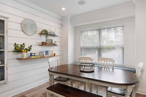 A dining area with a wooden table, white chairs, and a window with blinds.