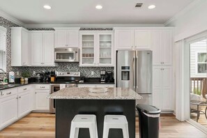 A modern kitchen with white cabinets, a granite countertop, stainless steel appliances, and a black trash bin.